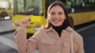 Kendine güveni tam genç bir kadın elinde boş sarı bir ulaşım kartı tutuyor. Arkasında bir belediye otobüsü var. Şehir içi taşıma kavramı..