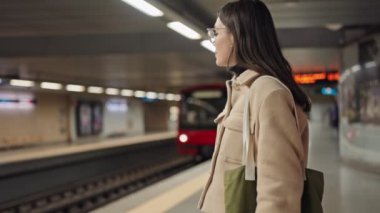 Bir metro istasyonunda sabırla bekleyen odaklanmış genç bir yetişkin yaklaşan treni bekliyor..