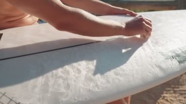 Dalgalarda sörf yapmaya hazırlanan sörf tahtasına ağda yapan bir sörfçünün yakın çekimi. Sörf tahtasını cilalamak sörfçünün kaymamasına yardımcı olur..