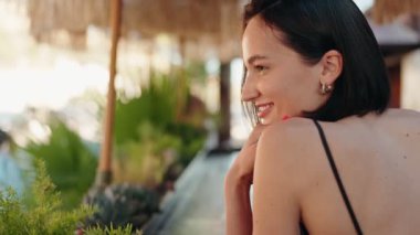 Genç bir kadın açık bir kafede oturuyor, gülümsüyor ve arkadaşlıktan ve sohbetten zevk alıyor. O mutlu ve arkadaşlarıyla iyi vakit geçiriyor..