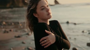 Gün batımında sakin bir sahilde yalnızlığı kucaklayan, gözleri kapalı bir kadın. Huzurlu sahil kıyısında bir sakinlik, kendi yansıması ve farkındalık hissi uyandırıyor..