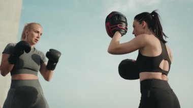 İki sportif kadın birlikte antrenman yapıyor, açık havada açık havada boks teknikleri uyguluyorlar, dayanıklılık ve zindelik sergiliyorlar..