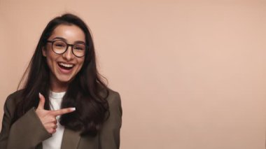 Gözlüklü neşeli iş kadını, bej arka plandaki fotokopi alanını işaret ediyor..