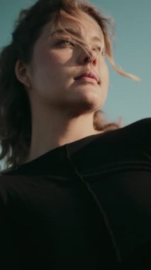 Düşük açılı bir çekim, genç bir kadının bakışları rüzgarda hafifçe savruluyor, düşüncelere dalma ve sükunet hissi veriyor..