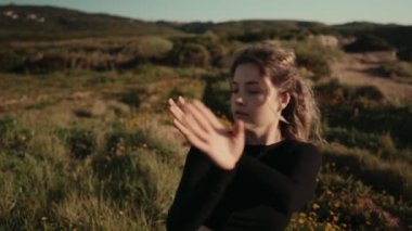 Genç bir kadın modern bir açık havada dans gösterisi yapıyor. Arka planda yeşil tepeler olan doğal bir ortamda sanat ve akışkan hareketler sergiliyor..