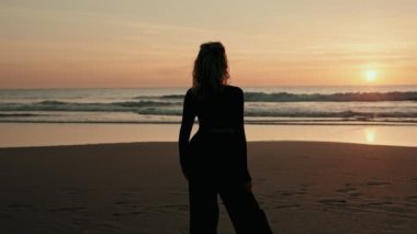 A silhouette of a person peacefully watching the sunset on a beach, evoking feelings of tranquility and reflection. The calm ocean waves add to the serene atmosphere.