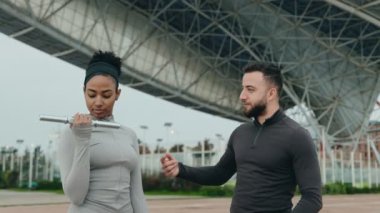 Sportif siyahi kadın, dış mekanda kişisel antrenörünün altında pazı egzersizi yapıyor..