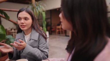 İki genç kadın, sıcak bir kafe ortamında kahve içerken sohbet etmekten hoşlanırlar. Hikayelerini ve kahkahalarını paylaşırlar..