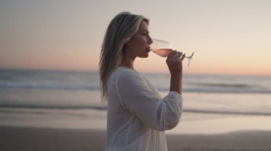 Genç bir kadın sahilde duruyor ve güneş ufukta batarken bir bardak şarabın tadını çıkarıyor. Sahne boyunca sıcak bir parıltı saçıyor. Bu bir huzur, rahatlama ve keyif hissi uyandırıyor..
