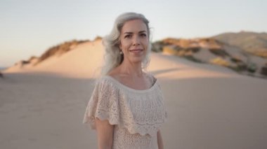 Mutlu olgun bir kadın, kumlu bir sahilde gün batımında huzurlu bir anın tadını çıkarıyor, zarif bir şekilde yaşlanıyor..