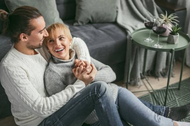 Gülümseyen bir çift, modern bir oturma odasında oturmuş sıcak bir anı kucaklıyor ve eğleniyorlar..