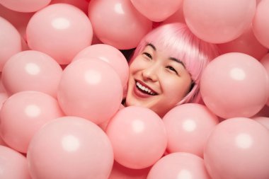 Joyful woman with pink hair smiling while surrounded by pink balloons, showcasing a fun and playful atmosphere. clipart