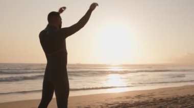 Dalgıç kıyafetli bir sörfçü gün doğumunda sahilde esneyerek sörf yapmaya hazırlanır. Huzurlu atmosferi ve doğanın güzelliğini kucaklıyor..