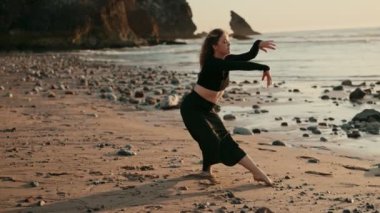 Günbatımında kayalık bir plajda dans eden çağdaş bir dansçı hareketin ve özgürlüğün özünü yakalar. Huzurlu okyanus arkaplanı sanatsal ifadeyi geliştirir.