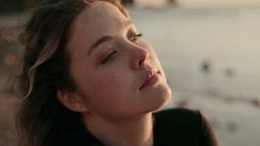 Gün batımını dikkatlice seyreden bir kadının yakın plan portresi. Suyun kenarında sakin ve düşünceli bir anı yakalıyor..