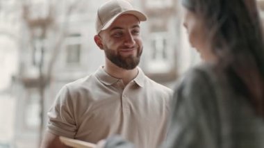 Neşeli, şapkalı bir erkek kurye güneşli bir günde dışarıdaki bir müşteriye zarf teslim eder ve etkin bir posta hizmeti sunar..