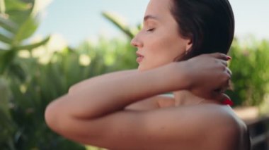 Genç bir kadın tropik bir tatilde elini kulağının arkasına koyarak saçını düzeltir. Güneşin tadını çıkarıyor..