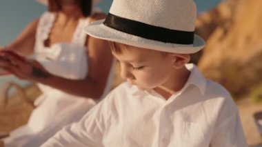 Bir anne ve oğlu güneşli bir plajda huzurlu bir pikniğin tadını çıkarırlar. İkisi de beyaz giyinmiş ve mutlu ve rahat görünüyorlar. Sevgi ve bağlantı duygusu aşikar..