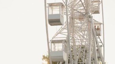 Dönme dolap gondolları bu yavaş çekim, alçak açılı videoda gün batımında güneşli bir lunaparkın üzerinde daireler çiziyor..