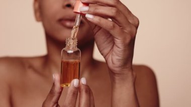 Serin, siyah bir kadının cildine serum yağı sürmek için damlatıcı kullanması, güzellik ve cilt rutinini gösteriyor..