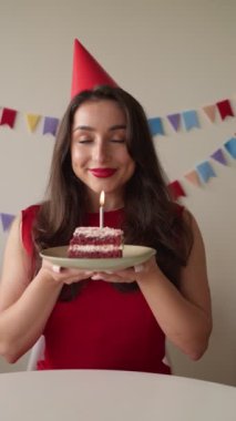 Parti şapkalı güzel bir kadın elinde yanan bir mumla kutlama pastası, gözleri kapalı, sessiz bir dilek diliyor..