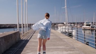 Yat limanındaki güneşli iskelede paten kayan genç bir kadın özgür ve maceraperest hissediyor..