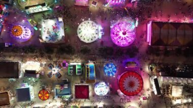 Geceleri kalabalık bir eğlence parkının havadan görünüşü, renkli ışıklar gezintileri ve eğlenceleri aydınlatıyor..