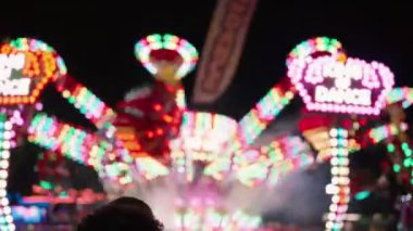 Gece bir lunapark gezisinin bulanık ışıkları ve ön planda bir kişinin silüeti. Eğlence, eğlence, çocukluk, yaz ve heyecan konseptleri için mükemmel.