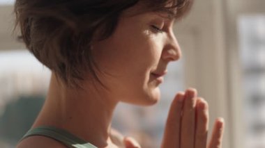 Gözleri kapalı, elleri dua pozisyonunda, güneş ışığında meditasyon yapan barışçıl bir kadının yakın çekimi. Farkındalık ve sükunet kavramı.