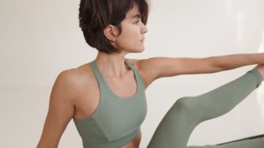 Yeşil aktif giysili, yoga esneme egzersizi yapan odaklanmış esmer kadın. Sağlıklı bir yaşam tarzı ve spor rutininin yakın çekim gösterimi.