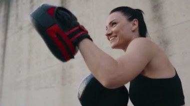 İki sportif kadın boks antrenmanı yapıyor. Koçun elinde boks bloknotlarıyla güçlü yumruklar atıyor..