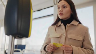 Odaklanmış genç bir kadın, bir ödeme terminalinde irtibatsız bir kartla tramvay yolculuğu için para ödüyor..