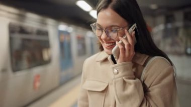 Genç, neşeli bir kadın metro trenini beklerken bir telefon görüşmesi yapıyor. Bağlantı ve şehir içi ulaşımı sinyalleri veriyor..