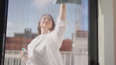 Ev işlerine odaklanmış bir kadın, güneşli bir pencereyi özenle temizliyor..