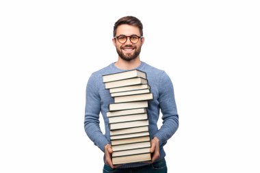 Gözlüklü neşeli bir adam uzun bir kitap yığını tutuyor, beyaz arka planı olan kapalı bir yerde duruyor. Görüntü, akademik veya mesleki bağlamda eğitim, öğrenme ve hazırlığı sembolize eder..