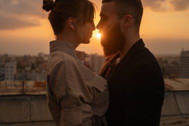 A couple shares an intimate moment on a rooftop during a vibrant sunset, expressing romance and connection. clipart