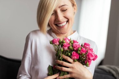 Elinde bir buket pembe gül tutan neşeli bir kadın, mutluluk ve minnettarlık iletiyor. Neşeli anları, aşkı ve çiçek hediyelerinin güzelliğini tasvir etmek için mükemmel..