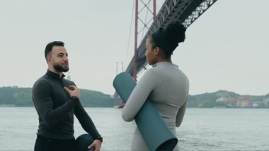 Bir erkek eğitmen, köprü yakınında egzersiz yapmadan önce Afrikalı bir Amerikalı kadınla egzersiz rutinleri hakkında konuşur..