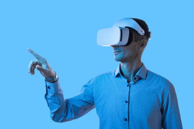 Profesyonel bir erkek dijital içerikle mavi bir arkaplan üzerinde sanal gerçeklik kulaklığı kullanarak etkileşime girer, modern teknoloji ve yenilikçi deneyimler sergiler..