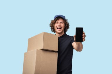 Kutuları tutan ve akıllı bir telefon gösteren hevesli teslimatçı, modern lojistik ve iletişimi canlı mavi bir arkaplanda resmediyor..