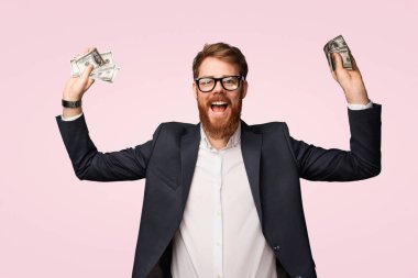 Resmi giyinmiş mutlu bir adam elinde bir tomar parayla neşe ve başarıyı ifade ediyor. Parlak pembe arka plan, finansal refahın iyimser ve neşeli atmosferini arttırır..