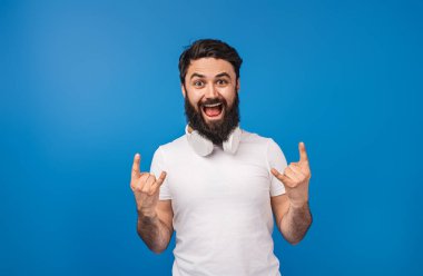 Beyaz kulaklık takan neşeli sakallı bir adam, rock el hareketleriyle neşeyi ifade eder. Canlı mavi arka plan, onun enerjik ve karizmatik kişiliğini vurguluyor.