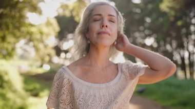 Gri saçlı olgun bir kadın gözlerini kapatır, derin derin nefes alır ve doğayla ve güneş ışığıyla bağlantı kurarken gülümser..