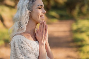Doğada sakin bir meditasyon seansından zevk alan memnun bir kadın. Açık havanın sükunetini ve sıcaklığını kucaklıyor, o anda huzur ve mutluluk buluyor..