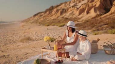 Güneş batarken, beyazlar içinde bir anne ve oğlu plaj pikniğinin tadını çıkarıyorlar. Yaz, birliktelik ve aile eğlencesi hissi uyandırıyorlar..