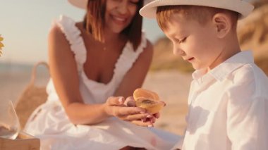 Bir anne ve küçük oğlu gün batımında plajda piknik yapıyorlar. Anne bir kayısı tutuyor ve oğlu bir ısırık alıyor..