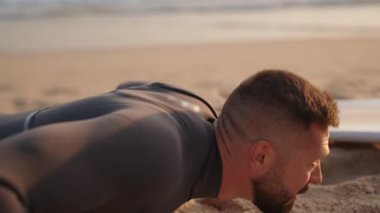 Bir sörfçü dalgalara çarpmadan önce ısınmak için plajda şınav çeker. Dalgıç kıyafeti giyiyor ve sabah sörf seansına hazırlanıyor..