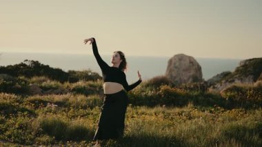 Zarif bir dansçı gün batımında, yemyeşil ve kayalık kayalıklarla çevrili manzarayla güzel bir dans eder..