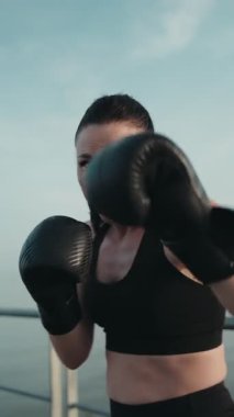 Boks eldiveni giyen, yumruk atan, gözlerinde kararlılık gösteren güçlü ve formda bir kadın..