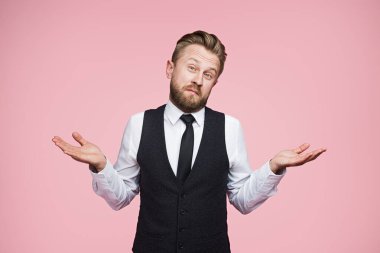 Profesyonel giyinmiş bir adam, parlak pembe bir arka plana karşı durarak omuz silkerek belirsizliğini ifade eder. Bu görüntü belirsizlik, merak ve düşüncenin bir arada tutulmasını sağlar.